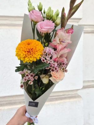 Bouquet of pink roses, yellow chrysanthemum, waxflowers and lisianthus held in light gray wrapping.