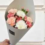 Bouquet of pink, peach, and white carnations wrapped in gray paper being held by a hand.