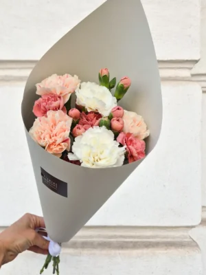 Bouquet of pink, peach, and white carnations wrapped in gray paper being held by a hand.